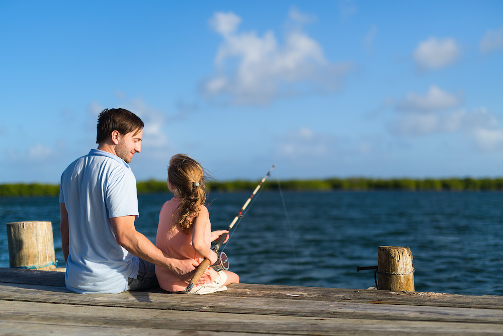 Family father and daughter fishing together from wooden jetty