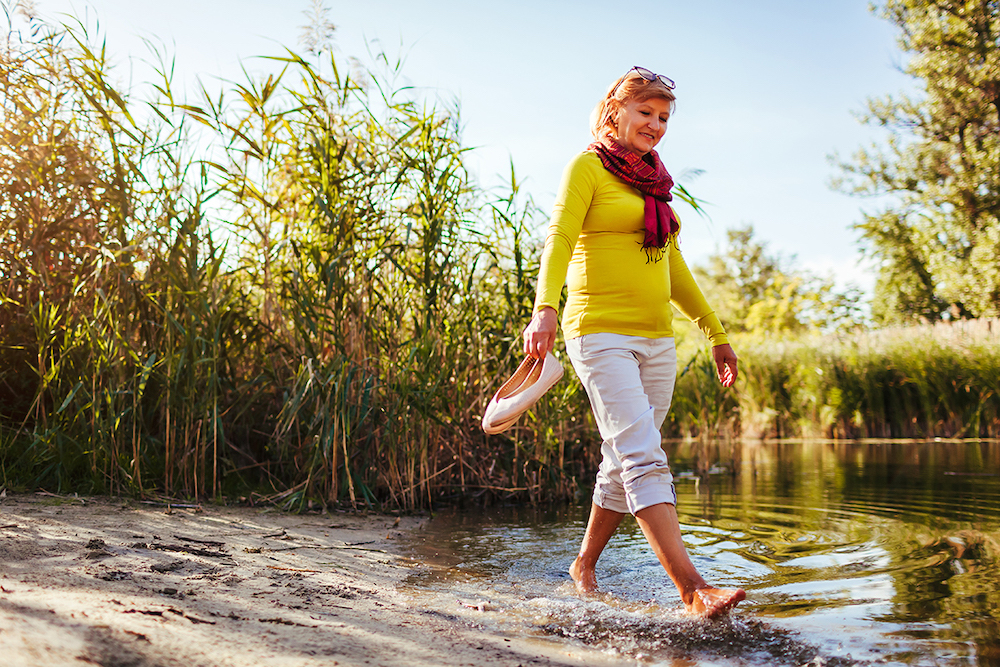 Middle-aged barefooted woman walking on river bank on autumn day. Senior lady having fun in the forest enjoying nature