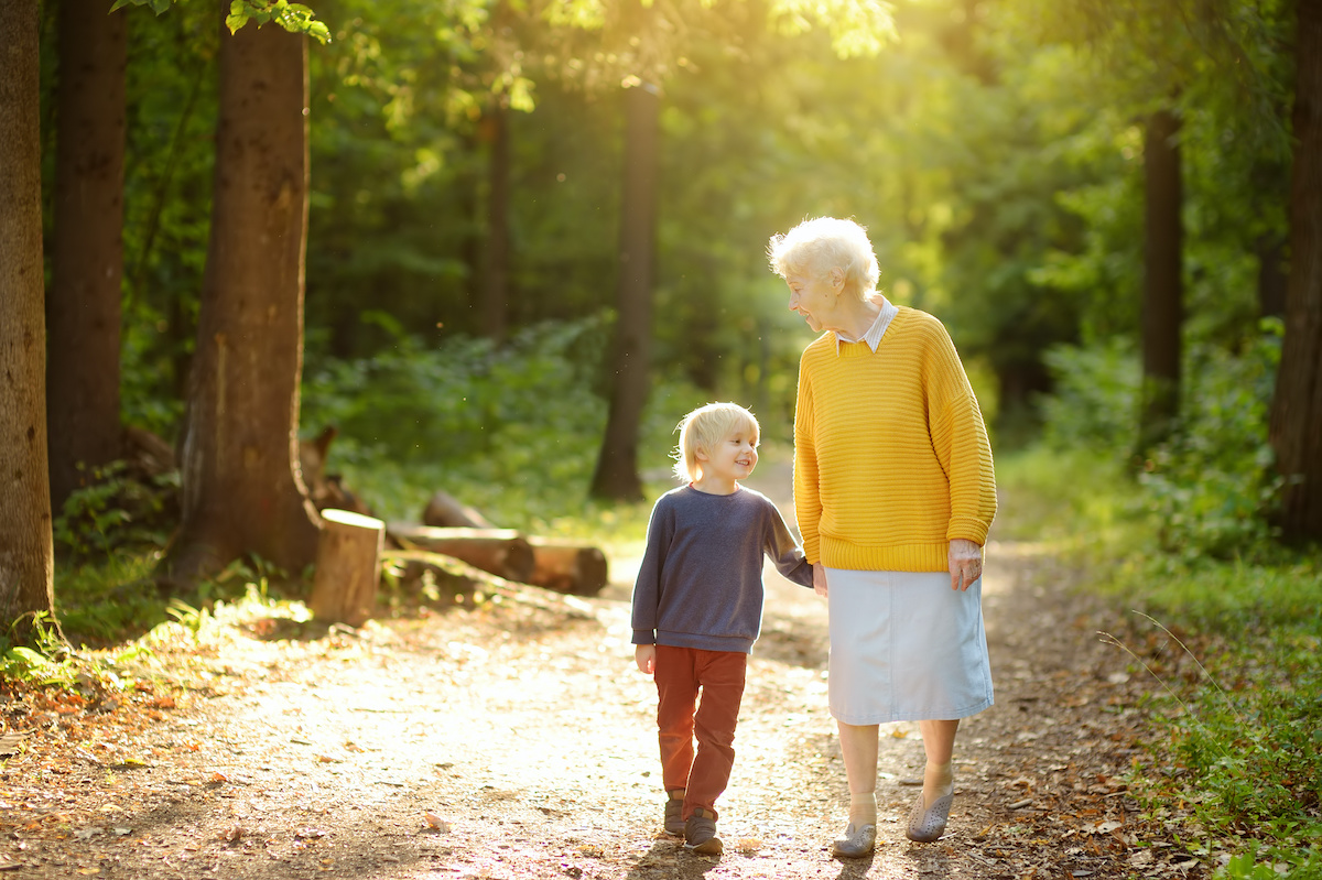 Elderly grandmother and her little grandchild walking together in sunny summer park. Friendship of grandma and grandson. Two generations of family.